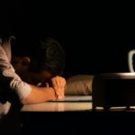 감정 억압이 위장과 흉부에 쌓이는 신체 감각의 정체 Man resting head on desk in dark room