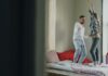 층간소음 걱정 없는 ‘방구석 댄스’ 홈트레이닝 꿀팁 Couple dancing joyfully on a bed near window.