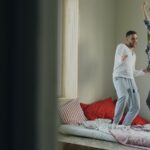 층간소음 걱정 없는 ‘방구석 댄스’ 홈트레이닝 꿀팁 Couple dancing joyfully on a bed near window.