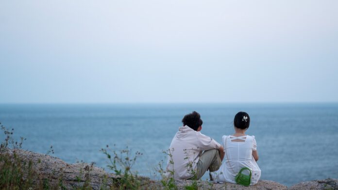 Photo by Vida Huang two people sitting on a rock looking out at the ocean